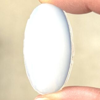 A soft contact lens held between two fingers, showing a pale blue-tinted lens edge-to-edge holder.