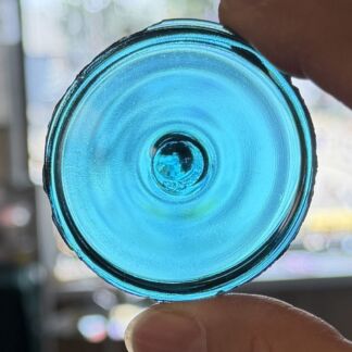 Close-up of the bottom of a blue glass bottle, held by a finger against a bright, out-of-focus background