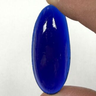 Cobalt blue glass disc held between fingertips against a white background.